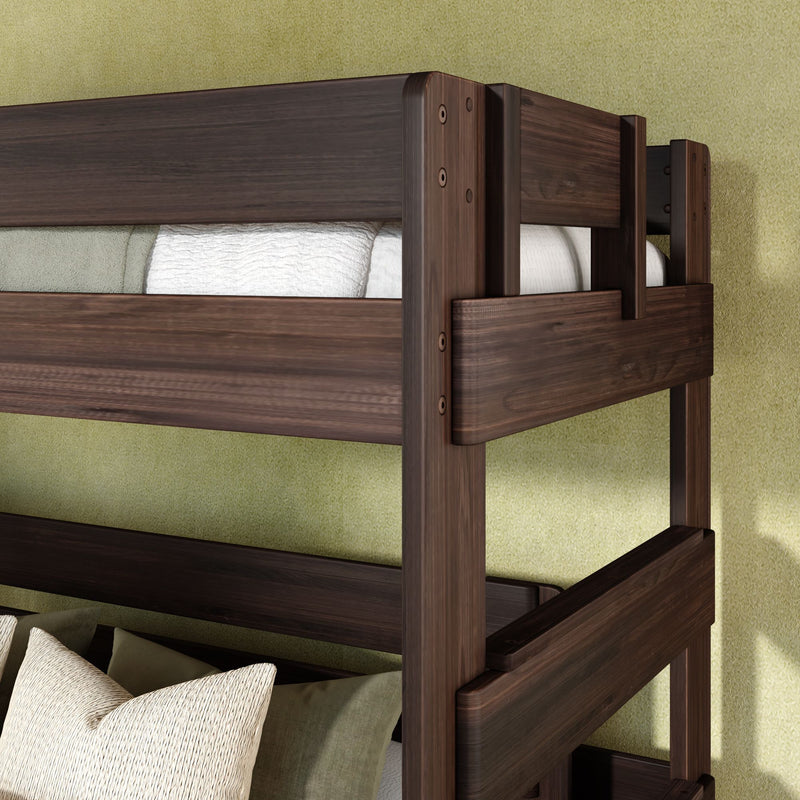 Close-up of solid wood bunk bed frame in dark walnut finish with guardrail and visible bolts, white linen mattress and pillows against a textured green wall