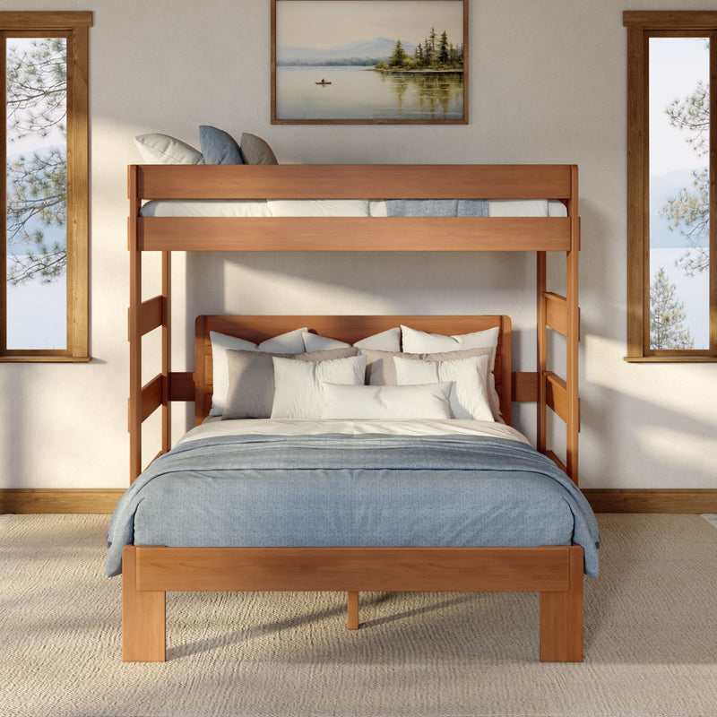 Light wood bunk bed with blue-gray bedding and layered pillows in a cozy neutral bedroom with framed lake painting and tall windows showing pine trees