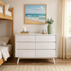 Modern white dresser with leafy decor in cozy bedroom setting with beach painting; stylish interior design.