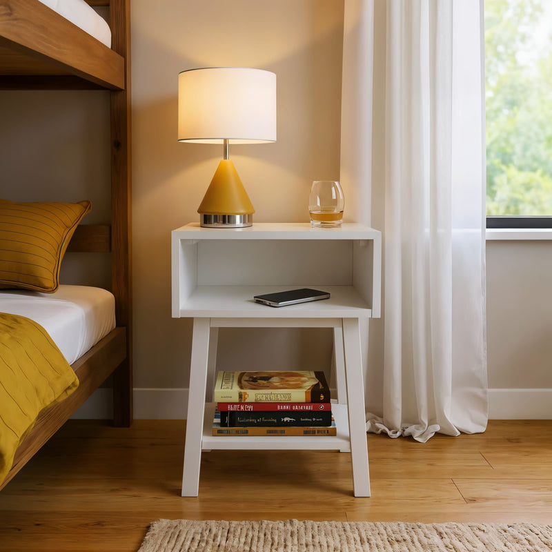 Cozy bedroom interior featuring a modern white nightstand with a warm yellow lamp, glass tumbler, smartphone, and stacked books near a bed with yellow bedding.