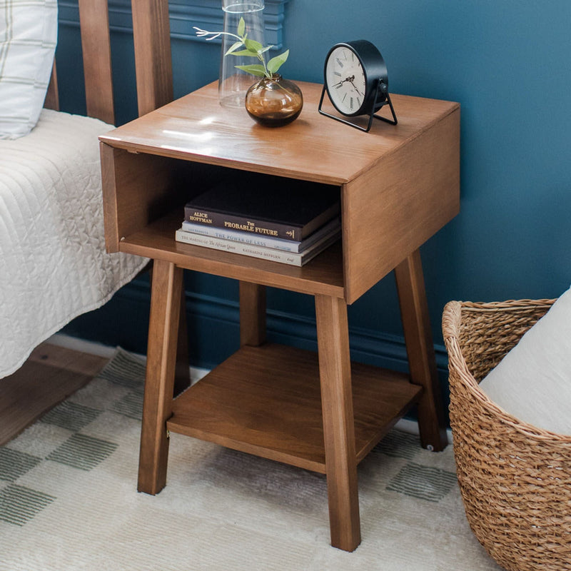 Wooden bedside table with books and a clock, placed next to a bed and wicker basket in a cozy bedroom.