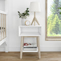 Stylish white bedside table with wooden legs, featuring a modern lamp, decorative plant vase, clock, and books, perfect for contemporary bedroom decor.