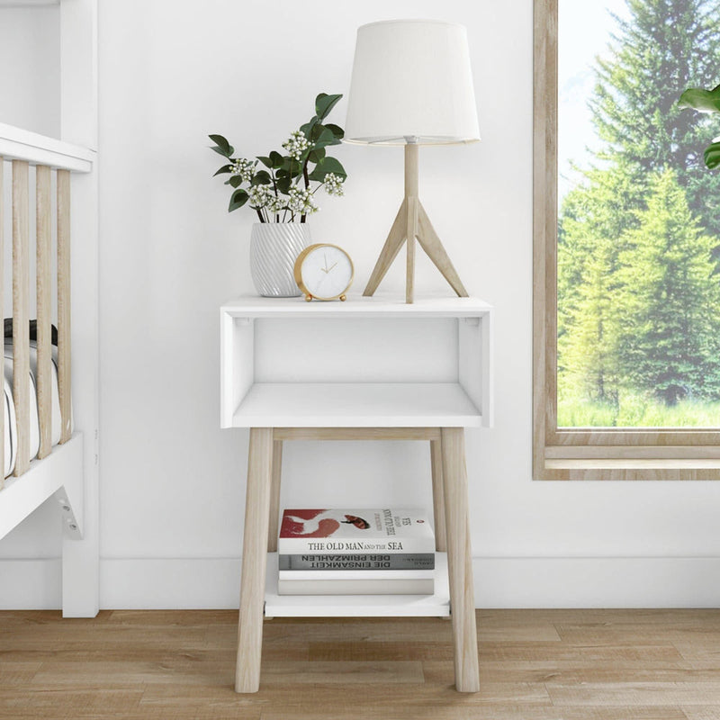 Stylish white bedside table with wooden legs, featuring a modern lamp, decorative plant vase, clock, and books, perfect for contemporary bedroom decor.