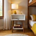 Modern bedroom with a stylish white nightstand featuring a book stack, table lamp, smartphone, and glass of water.