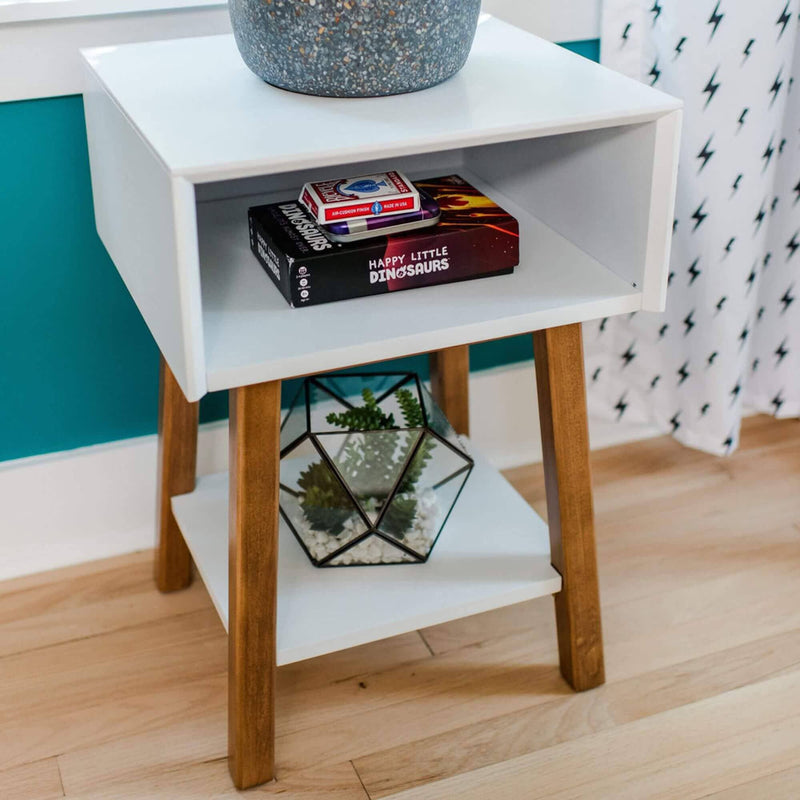 Modern white nightstand with wooden legs featuring a potted plant, a deck of playing cards, and a book on a teal background.