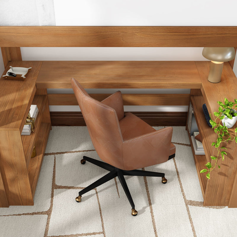 Modern home office workspace with camel leather swivel chair, L-shaped walnut desk with built-in shelves, brass-accented casters, table lamp, trailing potted plant and neutral geometric rug