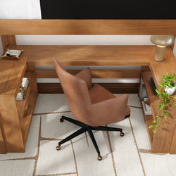Modern home office with brown leather swivel chair at a wooden L-shaped desk, brass table lamp, potted ivy, and white geometric rug