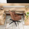 Modern home office workspace featuring a light wood L-shaped desk, tan leather swivel chair with black caster base, cream geometric rug, gold table lamp and potted trailing plant on open shelving