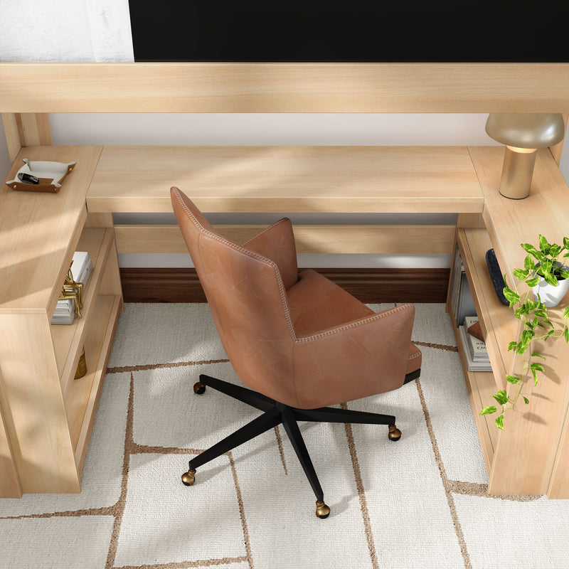 Modern home office workspace featuring a light wood L-shaped desk, tan leather swivel chair with black caster base, cream geometric rug, gold table lamp and potted trailing plant on open shelving