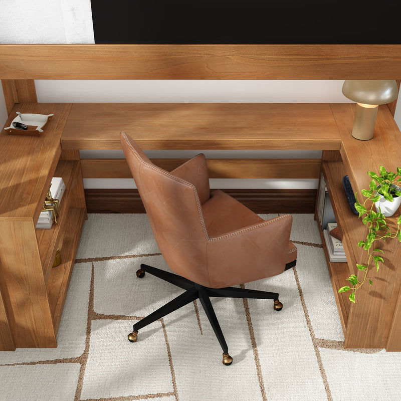 Modern home office workspace with tan leather swivel chair, wooden L-shaped desk with open shelves, brass-accented lamp and potted plant on a white geometric rug