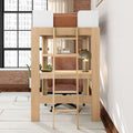 Wood loft bed with built-in desk and ladder, leather office chair, brass desk lamp, potted plants and exposed brick wall under large industrial window in a bright modern studio apartment