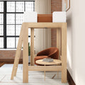 Wooden loft bed with ladder above cozy reading nook with rust velvet armchair, round coffee table, books, exposed brick and large windows