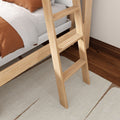 Light natural wood bunk bed ladder against hardwood floor with white bedding, rust-orange throw and neutral area rug