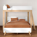 Modern wooden bunk bed with double lower bed and single upper bed, brown duvet and pillows, white headboards and ladder in a minimalist Scandinavian bedroom on hardwood floor