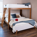 Modern wooden full-over-twin bunk bed with ladder, white and blue bedding and folded red towels on the made lower bed in a bright hardwood-floor bedroom