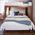 Modern wooden bunk bed with ladder and lower bed styled with blue and beige quilts and pillows, nightstand with lamp in a cozy hardwood-floor bedroom