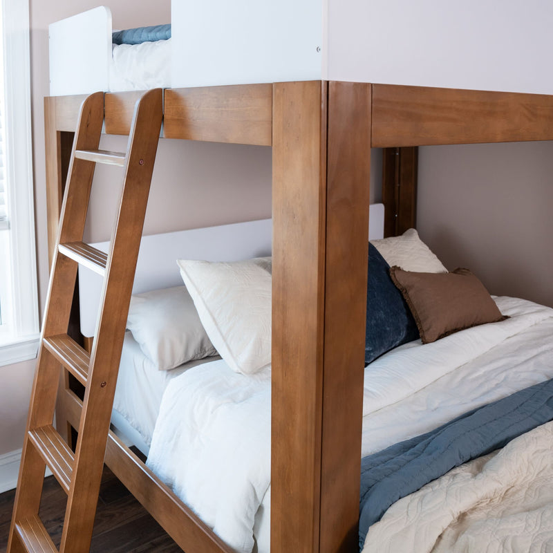 Light wood bunk bed with ladder, neatly made lower bed with white comforter, blue throw blanket and brown accent pillows.