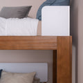 Solid wood twin-over-twin bunk bed corner with warm brown finish, white headboards, crisp white bedding and blue-gray pillows in a modern bedroom