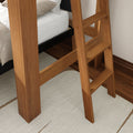 Close-up of solid wood ladder on a loft bed with white mattress and neutral rug on hardwood floor