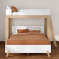 Modern wooden bunk bed with lower double bed and upper twin loft, white panels, rust-orange bedding and ladder on hardwood floor