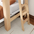 Close-up of natural wood bunk bed ladder beside white bed frame with rust bedding, beige rug and hardwood floor