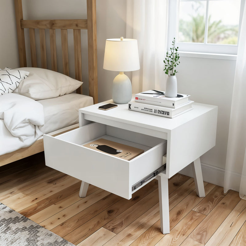 White modern nightstand with open drawer in cozy bedroom, featuring books, lamp, and smartphone on top.
