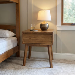 Mid-century modern wooden nightstand with lamp and glass of water next to a cozy bed in a neutral-toned bedroom.