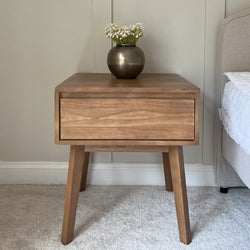 Mid-century modern wooden nightstand with drawer and vase of flowers, bedside table decor.
