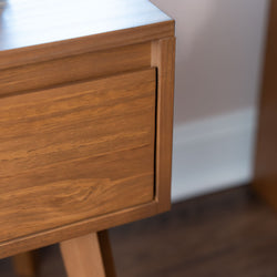 Mid-century modern walnut nightstand close-up showing warm wood grain, flush drawer front and tapered legs — minimalist bedside table