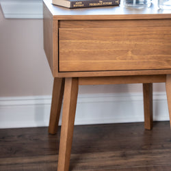 Mid-century modern walnut nightstand bedside table with single drawer and tapered legs, styled with book and glass vase on dark hardwood floor