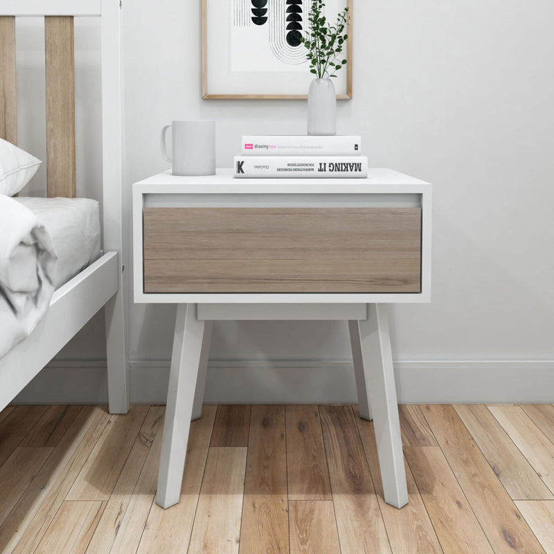 Modern white bedside table with wooden drawer, featuring a book, vase, and mug, in a minimalist bedroom setting.