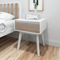 Modern white and wood nightstand with books and a plant in a minimalist bedroom.