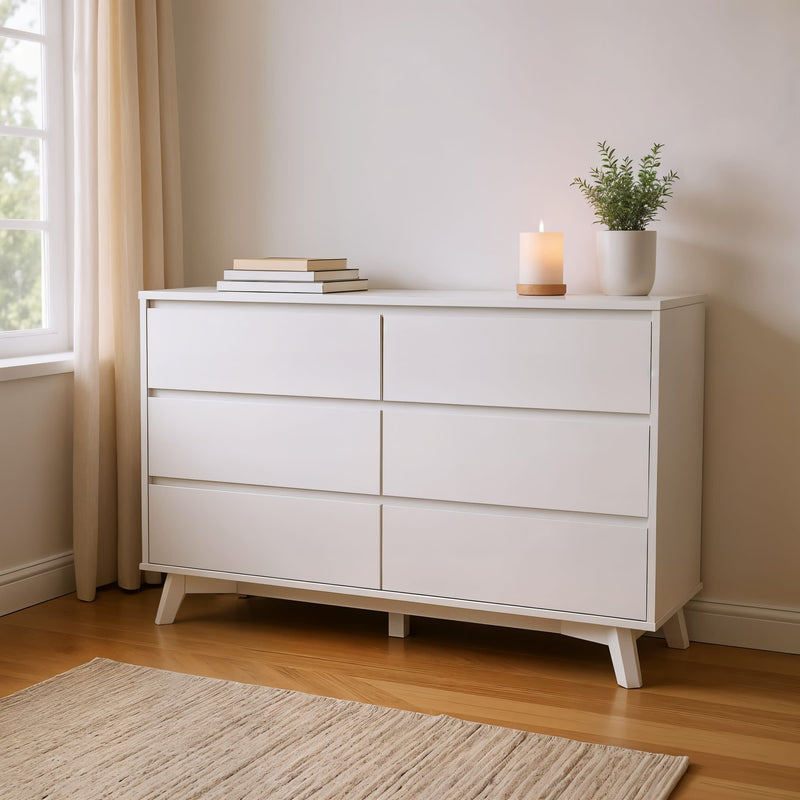White modern dresser with six drawers, styled with books, a lit candle, and a potted plant, positioned near a window in a cozy room.