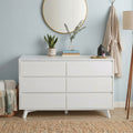 Modern white dresser with round gold mirror, snake plant in ceramic pot, eucalyptus in glass vase, stacked books, aromatherapy diffuser and hanging beige robe — bedroom decor