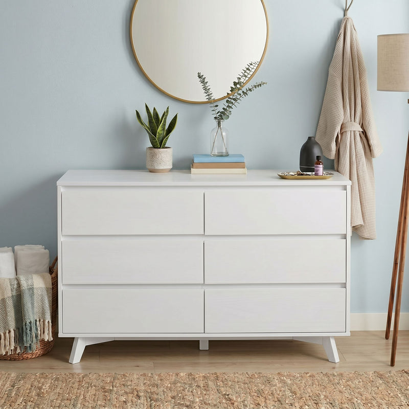 Modern white dresser with round gold mirror, snake plant in ceramic pot, eucalyptus in glass vase, stacked books, aromatherapy diffuser and hanging beige robe — bedroom decor
