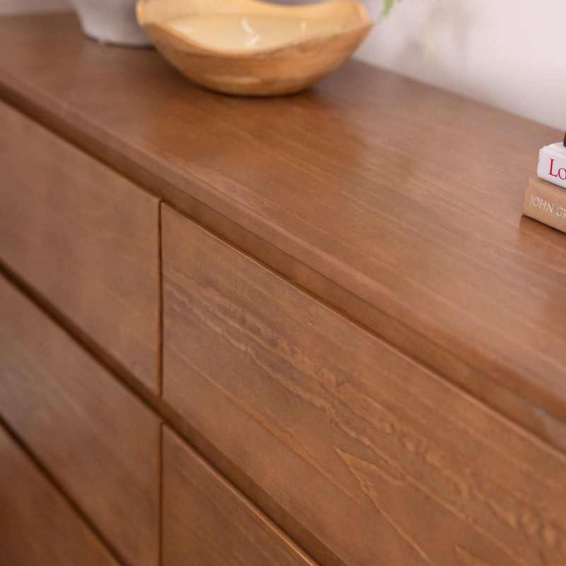 Mid-century modern wooden dresser close-up showing natural wood grain, recessed drawer fronts, and a decorative bowl with stacked books on top
