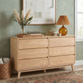 Mid-century modern natural wood dresser styled with amber glass lamp, pampas grass and eucalyptus vase, stacked books and ceramic bowls on rattan tray against sage green wall art, boho home decor