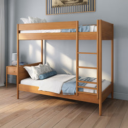 Two-tier wooden bunk bed with ladder, blue bedding and decorative pillows in a modern bedroom with wooden nightstand and hardwood floors