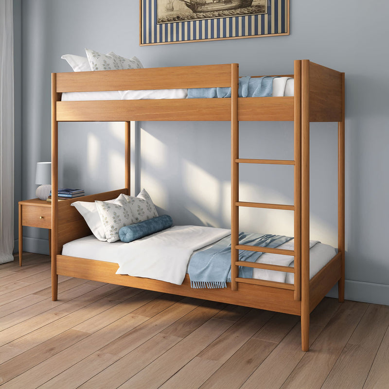 Two-tier wooden bunk bed with ladder, blue bedding and decorative pillows in a modern bedroom with wooden nightstand and hardwood floors
