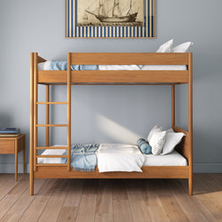Modern solid wood bunk bed with ladder, blue and white bedding and decorative pillows in a minimalist coastal-style bedroom
