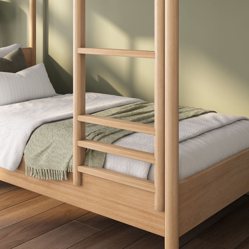 Close-up of a light natural wood platform canopy bed with ladder-style posts, white quilted bedding and a green textured throw on hardwood floors in a minimalist Scandinavian bedroom.