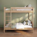 Modern light wood twin-over-twin bunk bed with white bedding, green throw and pillows in a kids' room with sage green wall and hardwood floor