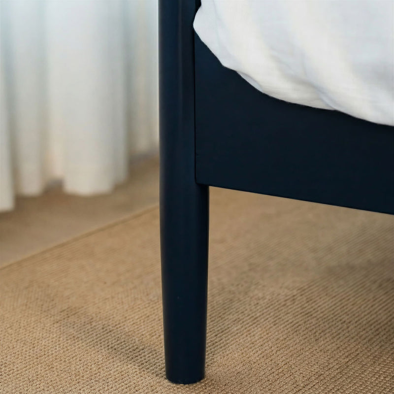 Close-up of black bed frame leg on beige woven jute rug with white bedding and minimalist bedroom decor
