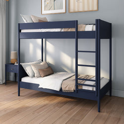 Modern navy blue wooden bunk bed with ladder in a minimalist kids' bedroom, lower bed dressed with beige throw and pillows, nightstand with lamp on hardwood floor
