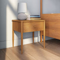 Mid-century modern wooden nightstand with single drawer, textured table lamp and stacked books beside bed in minimalist bedroom
