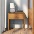 Mid-century modern wooden bedside nightstand with single drawer, white textured table lamp and stacked design books in a bright bedroom