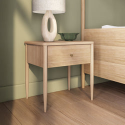 Minimalist mid-century modern light oak nightstand bedside table with single drawer, sculptural ceramic lamp and green decorative bowl against a sage green wall in a Scandinavian bedroom interior