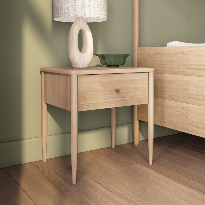 Minimalist mid-century modern light oak nightstand bedside table with single drawer, sculptural ceramic lamp and green decorative bowl against a sage green wall in a Scandinavian bedroom interior