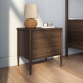 Mid-century modern walnut two-drawer nightstand with brass knobs, woven rattan table lamp and decorative tray with candle, styled bedroom interior on hardwood floor