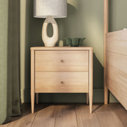 Light oak two-drawer wooden nightstand with linen lamp and green ceramic bowl against a sage-green wall — modern Scandinavian bedside table bedroom decor